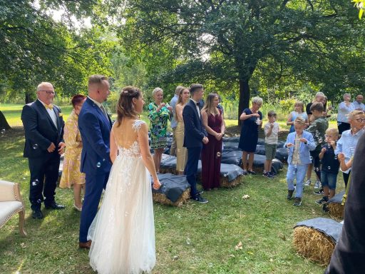 Freie Trauungszeremonie Hochzeitszeremonie im Freien, umgeben von Gästen in festlicher Kleidung.